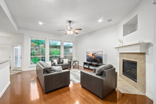 living room with a ceiling fan, visible vents, a fireplace, wood finished floors, and baseboards