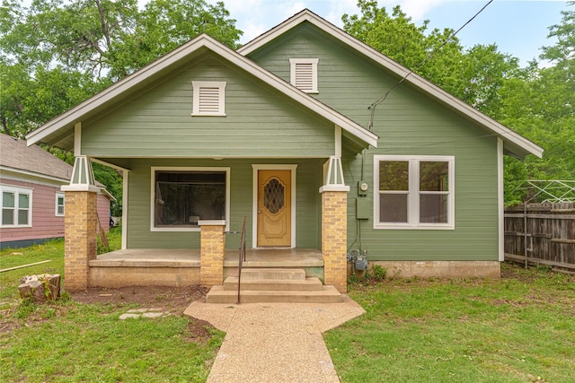 bungalow-style home featuring covered porch, fence, and a front yard