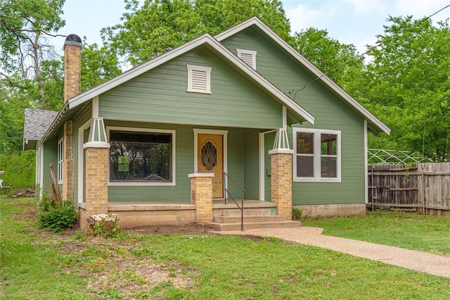 view of front of property with a front yard, fence, covered porch, and a chimney