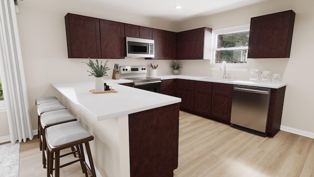 kitchen featuring a sink, stainless steel appliances, a kitchen bar, and light wood-style flooring
