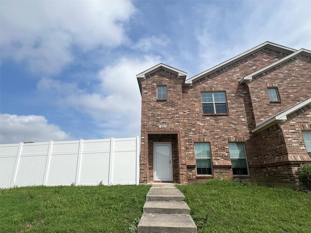 traditional home featuring brick siding, a front lawn, and fence