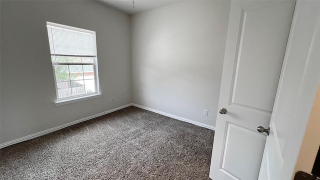 unfurnished room with baseboards and dark carpet