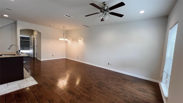unfurnished living room featuring visible vents, arched walkways, a sink, dark wood finished floors, and ceiling fan with notable chandelier