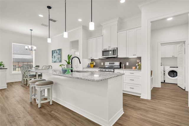 kitchen featuring washer / clothes dryer, range, stainless steel microwave, light wood finished floors, and a notable chandelier