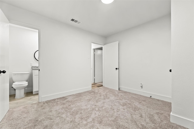 unfurnished bedroom featuring visible vents, baseboards, ensuite bath, and light colored carpet