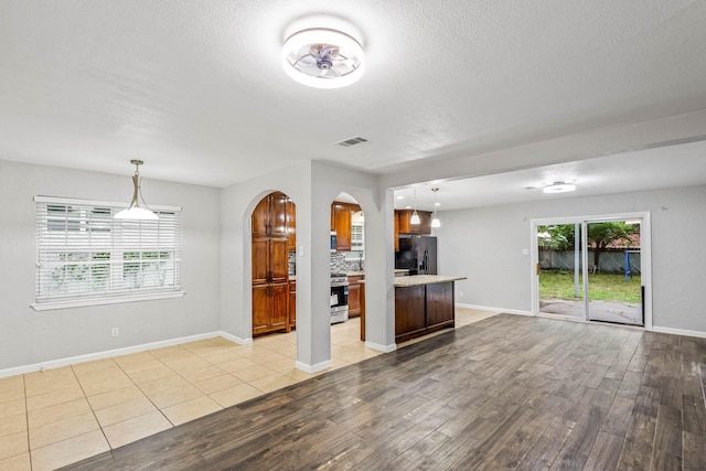unfurnished living room featuring a textured ceiling, visible vents, arched walkways, baseboards, and light wood finished floors