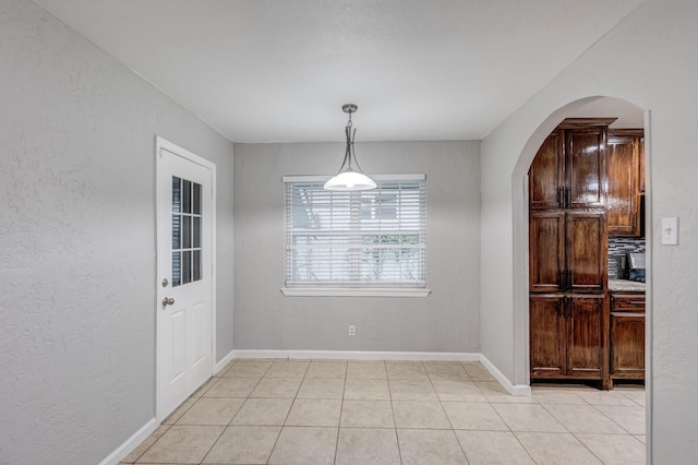 unfurnished dining area with arched walkways, baseboards, a textured wall, and light tile patterned floors