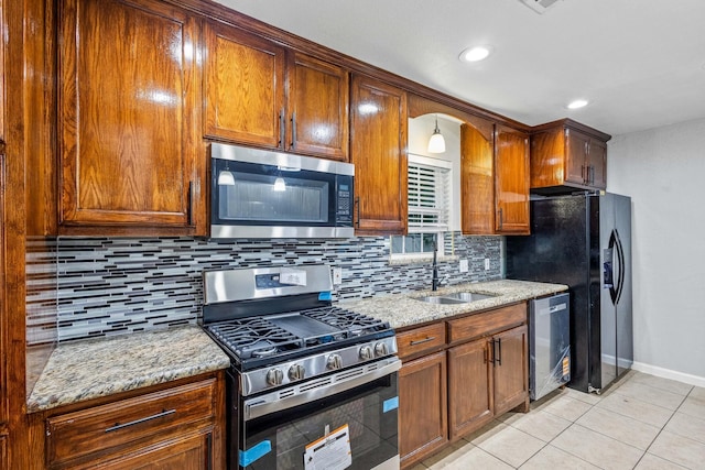 kitchen featuring appliances with stainless steel finishes, light stone counters, a sink, baseboards, and tasteful backsplash