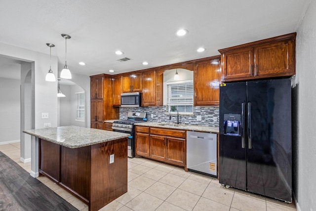 kitchen featuring decorative backsplash, appliances with stainless steel finishes, arched walkways, a sink, and light stone counters