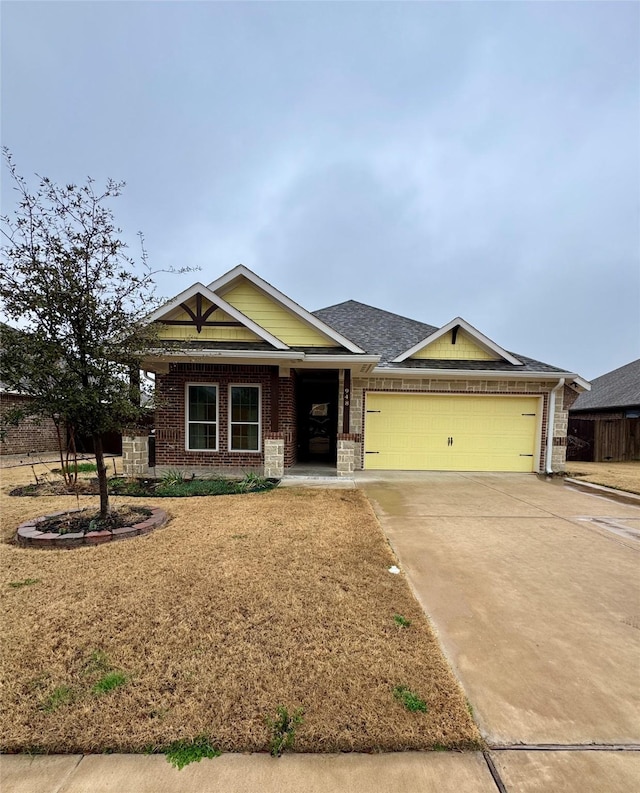 craftsman-style home featuring a garage, brick siding, a front lawn, concrete driveway, and a shingled roof