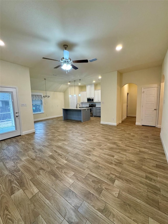 unfurnished living room featuring light wood-style floors, arched walkways, baseboards, and a ceiling fan