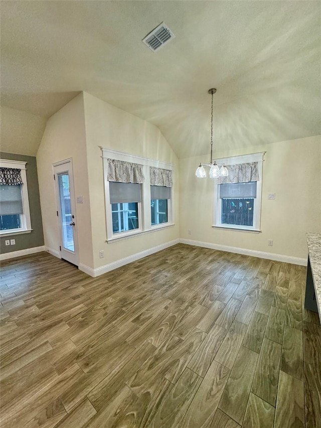 unfurnished dining area featuring baseboards, vaulted ceiling, wood finished floors, and visible vents