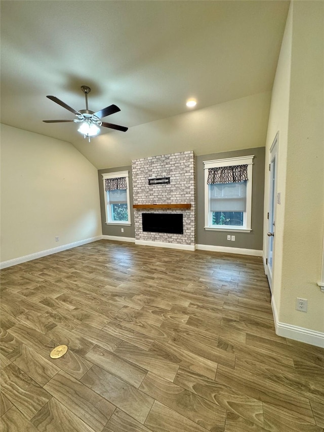 unfurnished living room featuring ceiling fan, a fireplace, baseboards, wood finished floors, and lofted ceiling
