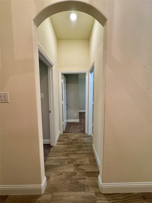 corridor with baseboards, arched walkways, a textured wall, and wood finished floors