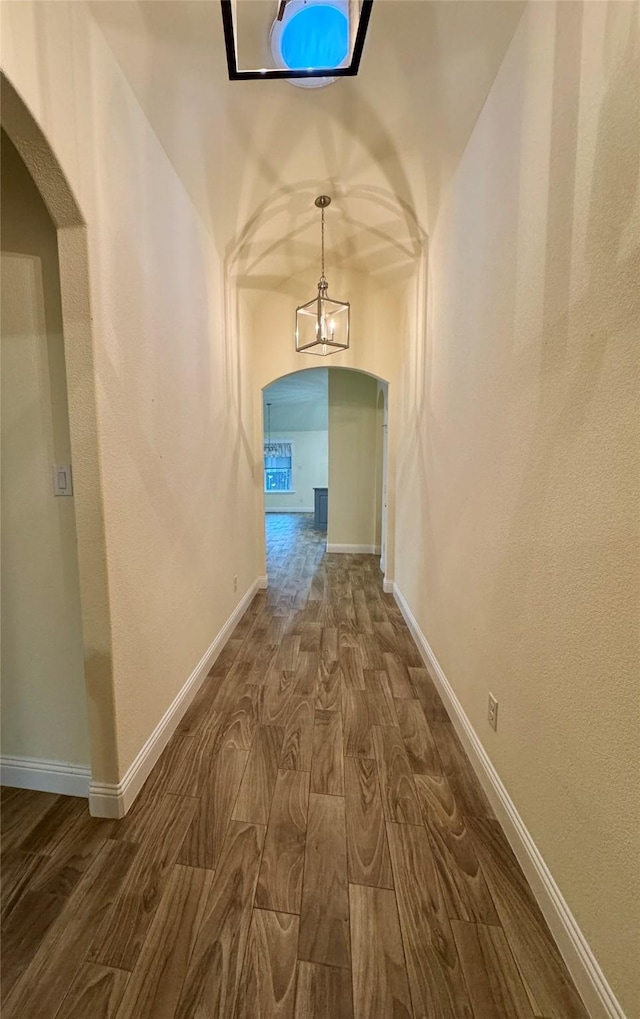 hall with arched walkways, baseboards, dark wood-style floors, and a notable chandelier