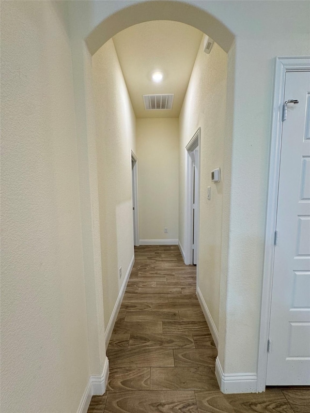 hallway featuring arched walkways, baseboards, visible vents, and wood finished floors