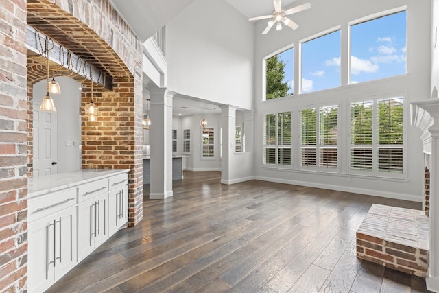 821 High Willow Dr, Prosper, TX 75078 - unfurnished living room featuring a ceiling fan, baseboards, dark wood-style floors, a high ceiling, and ornate columns