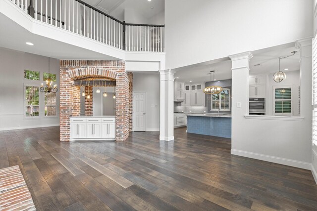 821 High Willow Dr, Prosper, TX 75078 - unfurnished living room featuring baseboards, a high ceiling, dark wood-style floors, ornate columns, and a notable chandelier