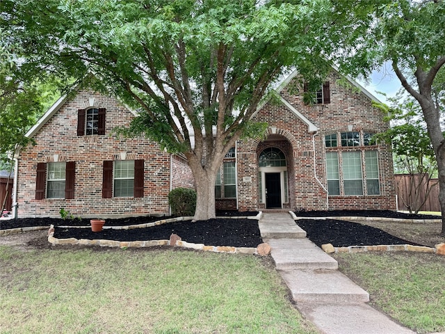 view of front facade featuring brick siding, fence, and a front lawn