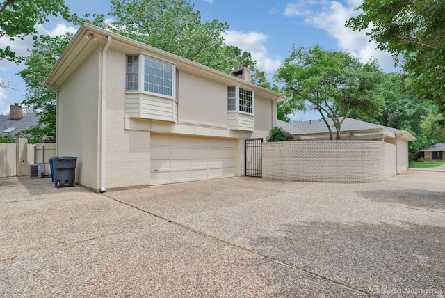 view of side of property featuring central AC unit, a gate, brick siding, fence, and concrete driveway