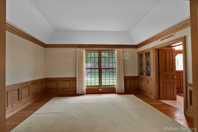 unfurnished room featuring visible vents, wood finished floors, lofted ceiling, and a wainscoted wall