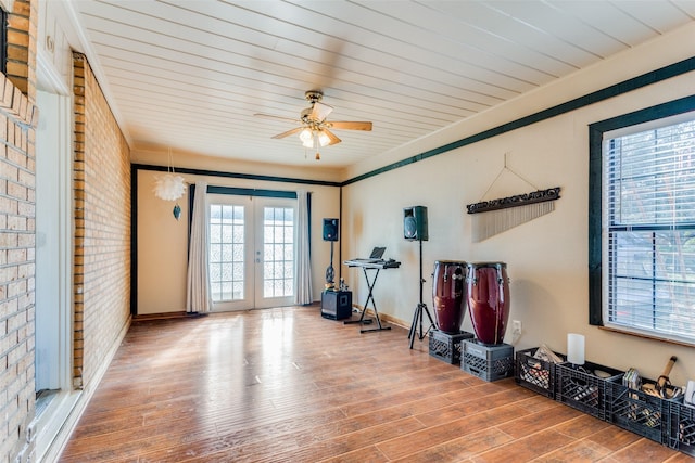 exercise room with wood finished floors, ceiling fan, french doors, and brick wall