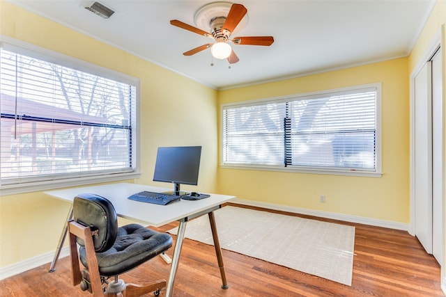 home office featuring a ceiling fan, visible vents, wood finished floors, baseboards, and ornamental molding