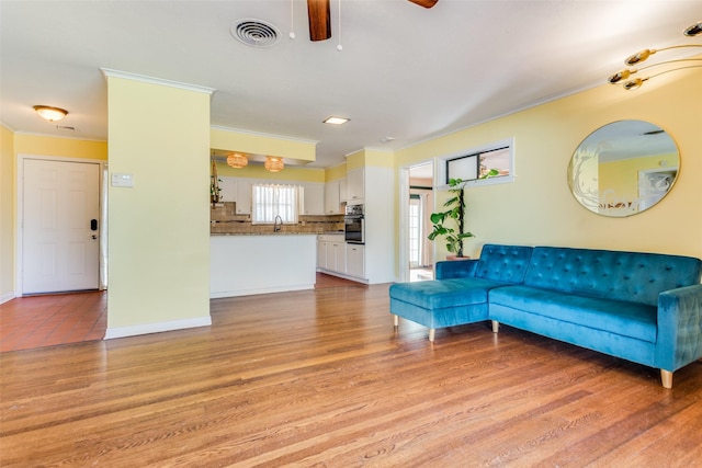 living room featuring a ceiling fan, visible vents, ornamental molding, and light wood-type flooring
