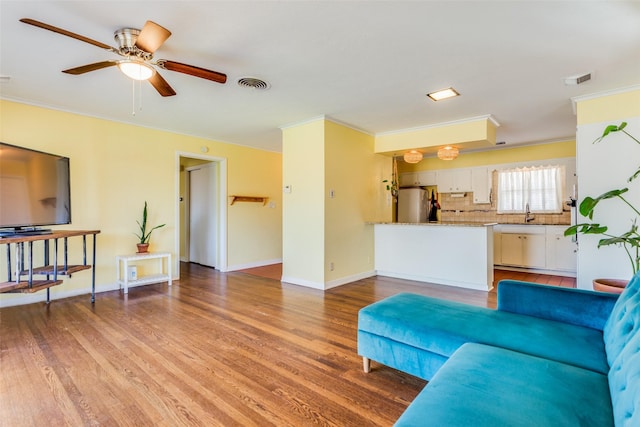 living room with a ceiling fan, visible vents, crown molding, baseboards, and light wood finished floors