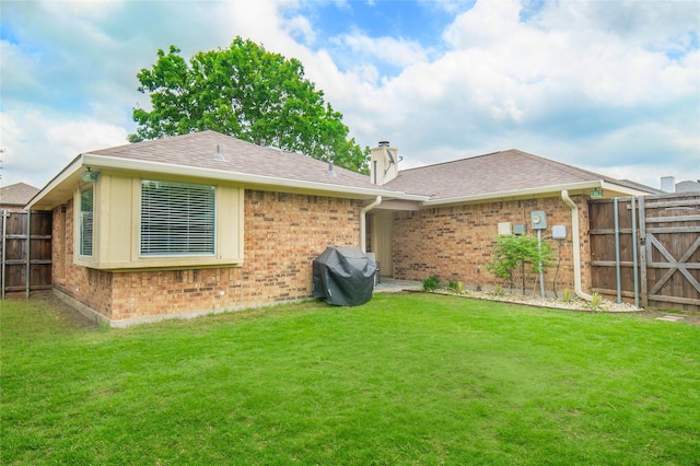 back of house featuring fence, roof with shingles, brick siding, a chimney, and a yard