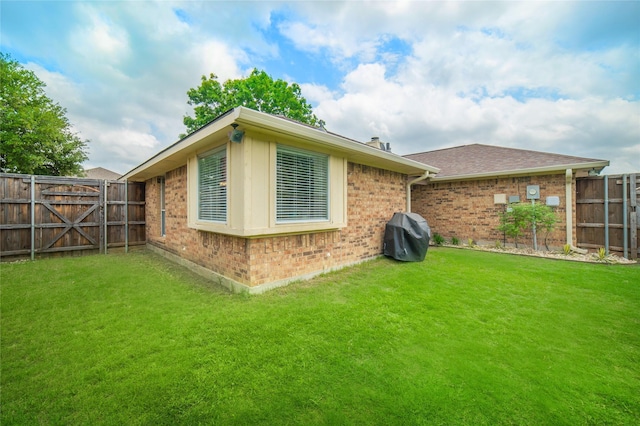 view of side of home with a lawn, brick siding, and a fenced backyard