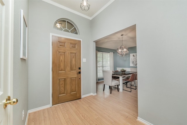 foyer entrance with baseboards, an inviting chandelier, ornamental molding, and light wood-style floors
