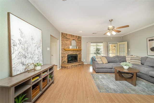 living area with a ceiling fan, ornamental molding, light wood finished floors, and a fireplace