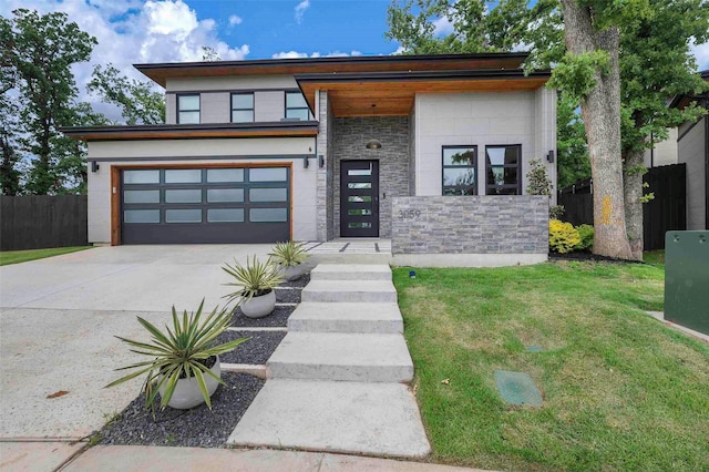 contemporary house with driveway, fence, a front lawn, an attached garage, and stone siding