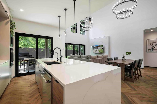 kitchen featuring appliances with stainless steel finishes, a sink, a chandelier, a towering ceiling, and pendant lighting