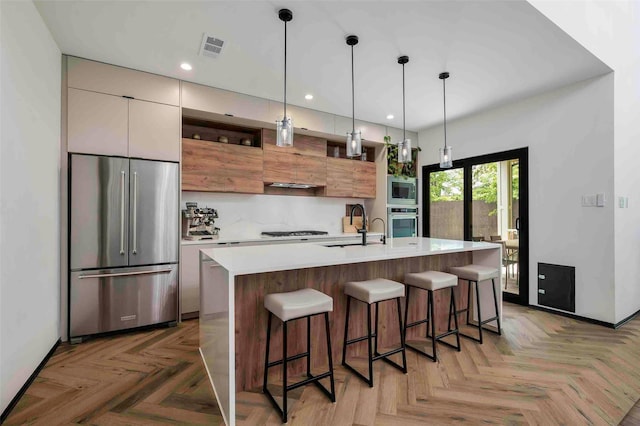 kitchen with modern cabinets, wall chimney range hood, light countertops, a sink, and appliances with stainless steel finishes