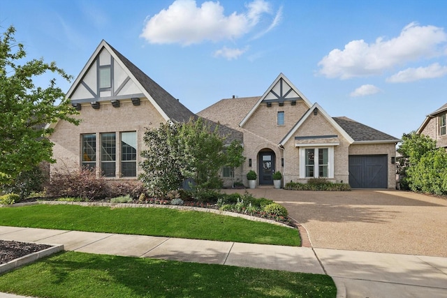 english style home featuring brick siding, a garage, a front lawn, and driveway