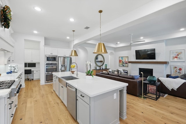 kitchen with a sink, light wood-style flooring, stainless steel appliances, open floor plan, and visible vents