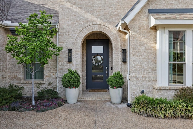 doorway to property featuring brick siding and roof with shingles