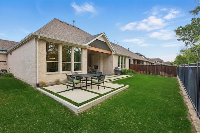 back of house with roof with shingles, a lawn, brick siding, a fenced backyard, and a patio