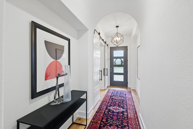 entryway with arched walkways, a barn door, and light wood finished floors