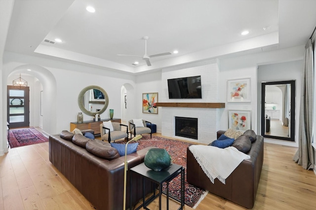 living area featuring arched walkways, recessed lighting, light wood-style flooring, and a raised ceiling