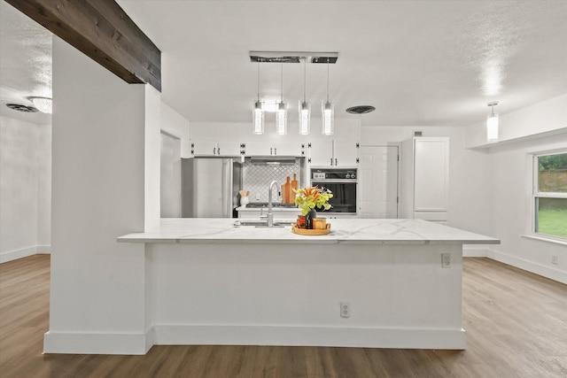 kitchen featuring baseboards, stainless steel refrigerator, black oven, and wood finished floors