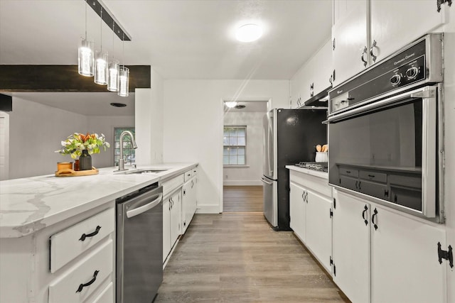 kitchen with a sink, white cabinets, light wood finished floors, a peninsula, and stainless steel appliances