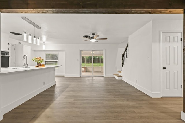 unfurnished living room featuring wood finished floors, baseboards, ceiling fan, stairway, and a sink