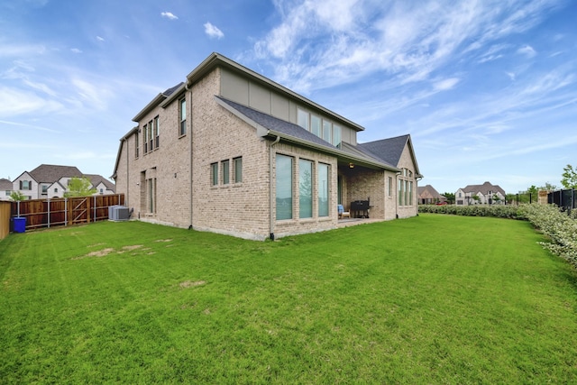 rear view of property with a lawn, brick siding, cooling unit, and a fenced backyard
