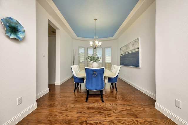 dining space with baseboards, dark wood finished floors, a tray ceiling, and a chandelier