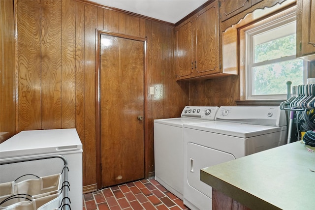 clothes washing area featuring cabinet space, independent washer and dryer, brick floor, and wooden walls