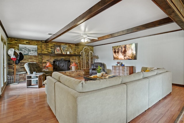 living area featuring beamed ceiling, light wood-style flooring, a wood stove, and brick wall