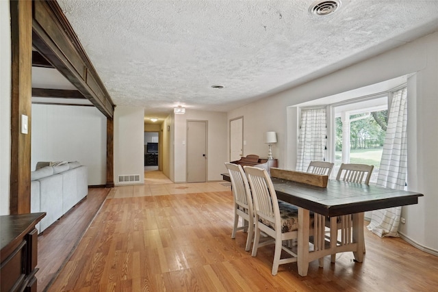 dining area featuring light wood-style floors, a textured ceiling, and visible vents
